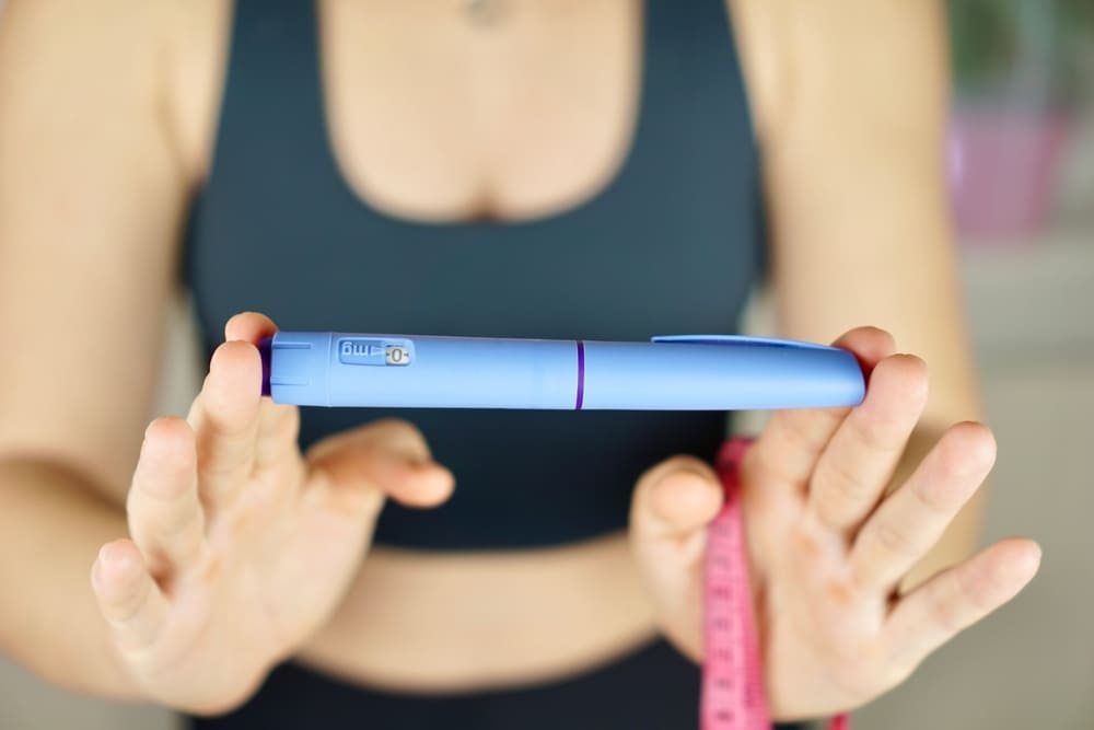 Fit woman holding GLP-1 injection pen with measuring tape, representing personalized weight loss treatment options.