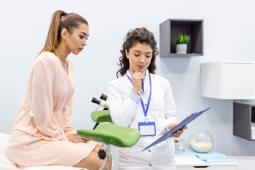 Female doctor discussing Pap smear frequency with patient during gynecologic wellness exam in a clinic setting.