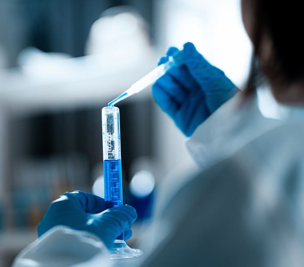 Lab technician wearing gloves inspecting blue liquid sample in test tube during initial accessioning process