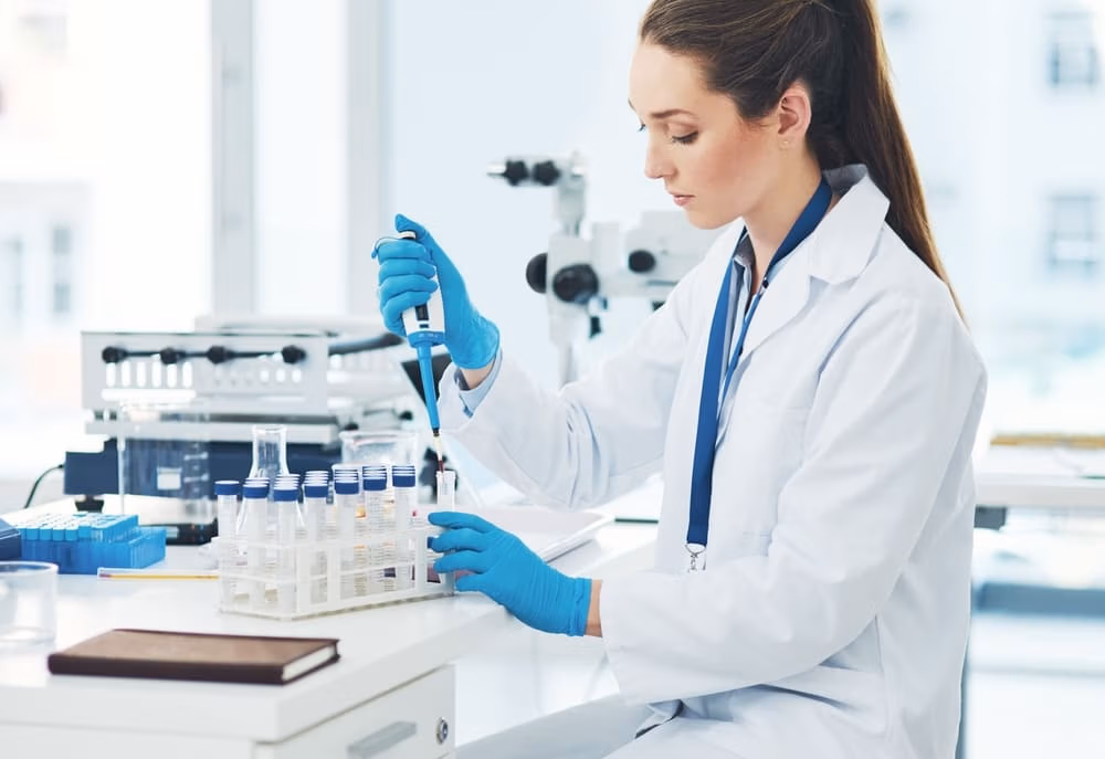 Female lab technician wearing gloves labeling test tubes during sample collection process in a bright laboratory